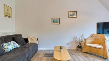 A modern living room with a dark sofa, a wooden coffee table, a wicker chair, and two framed pictures on the wall.