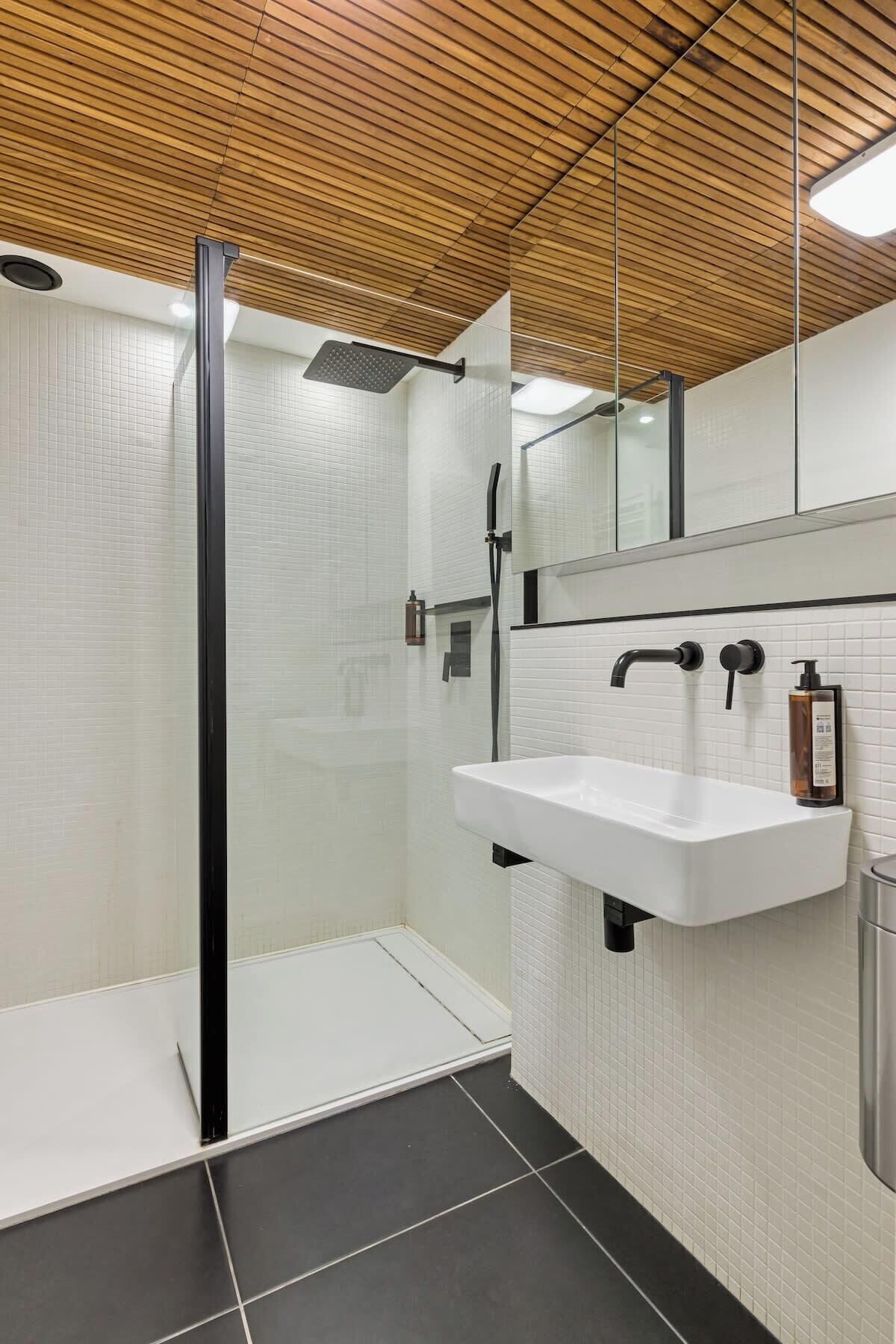 A modern bathroom with a glass-enclosed shower, a white sink, and a wooden ceiling.