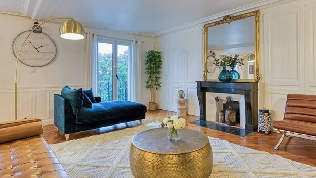 A living room with a dark blue sofa, a gold round coffee table, and a large mirror above a fireplace.