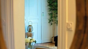 A view through a mirror reflecting a room with a white door, a plant, and a table with a vase of flowers.