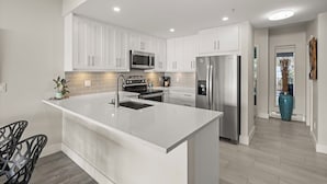 A modern kitchen with white cabinetry, stainless steel appliances, and a central island. - Stunning waterfront apartment - wake up and fall asleep listening to the ocean (Delta)