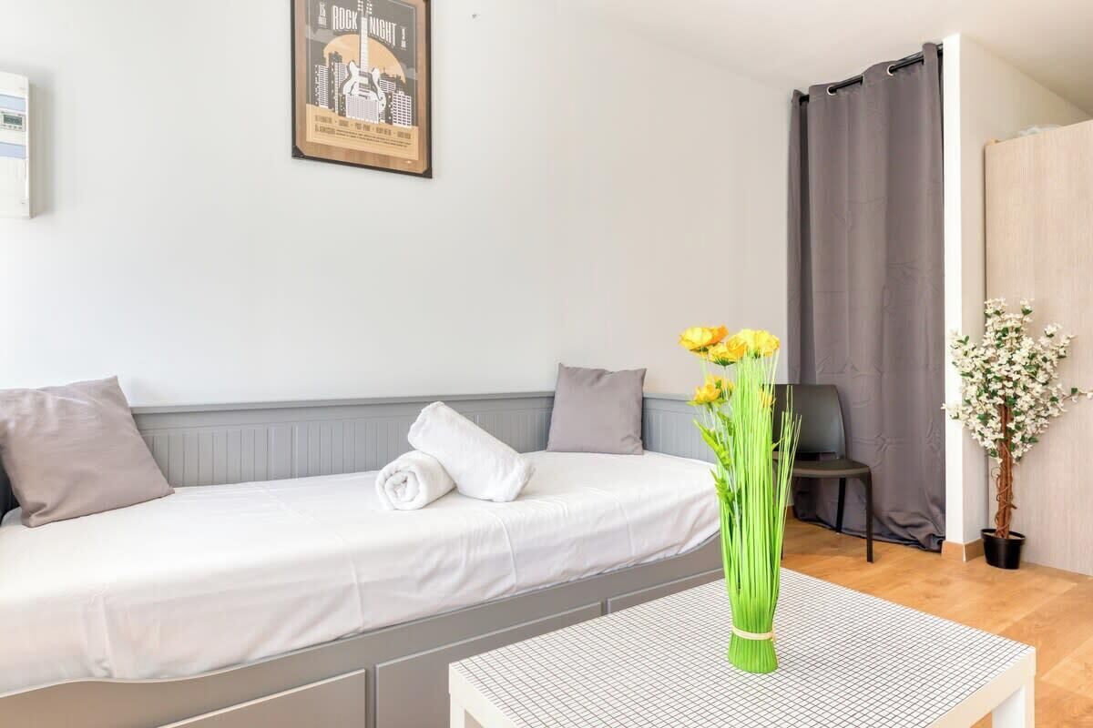 Een netjes ingerichte slaapkamer met een bed, een klein tafeltje met een bloevas, een stoel en een kamerplant.