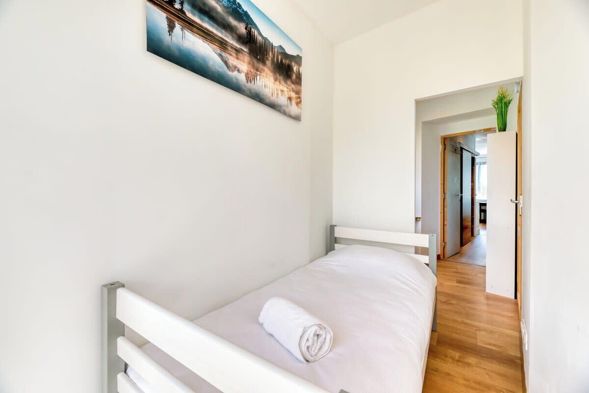 A single bed with a rolled white towel, a white headboard, and a painting of a mountain landscape on the wall.