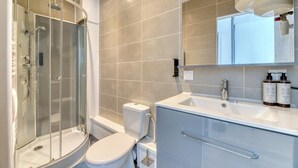 A modern bathroom with a glass-enclosed shower, a white toilet, and a vanity with a mirror and two bottles of shampoo. - Rollin, appartement 3 personnes avec Netflix au calme ! (Sotteville-lès-Rouen)