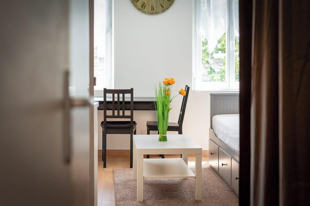 Une chambre à coucher avec un lit, une petite table sur laquelle est posé un vase de fleurs et une chaise.