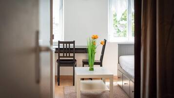 Une chambre à coucher avec un lit, une petite table sur laquelle est posé un vase de fleurs et une chaise.