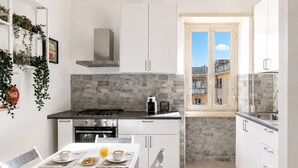 Una cucina moderna con mobili bianchi, piano cottura a gas, forno e una finestra con vista sugli edifici.