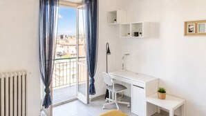 Una camera da letto moderna con una scrivania, una sedia e vista sulla città da un balcone.