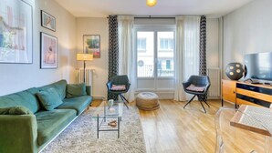 Una sala de estar moderna con un sofá verde, dos sillones, una mesita de centro y un televisor sobre un mueble de madera.