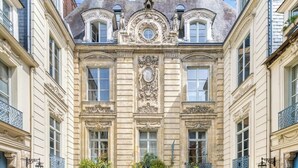 Un bâtiment historique doté d’une cour pavée, de détails architecturaux raffinés et de fenêtres disposées de manière symétrique.