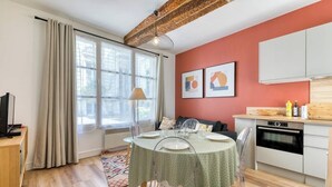 Un espace de vie compact comprenant un coin repas, une kitchenette et une grande fenêtre avec des rideaux.