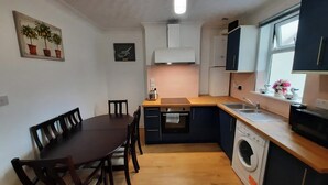 Cocina compacta con mesa, sillas, lavadora y ventana decorada con cisnes.