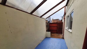 Un espacio reducido y cerrado con piso azul, pared blanca y una puerta de madera que da a un área exterior.