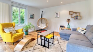 A modern living room with a yellow armchair, a grey sofa, a wooden coffee table, a wicker chair, and a potted plant.