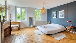 A bedroom with a large bed, a fireplace, a window, and a hanging light fixture.