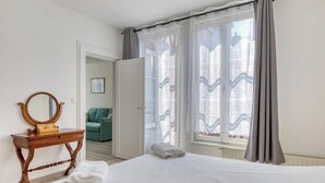 Habitación de hotel con cama, cómoda de madera con espejo, silla verde y ventana con cortinas.