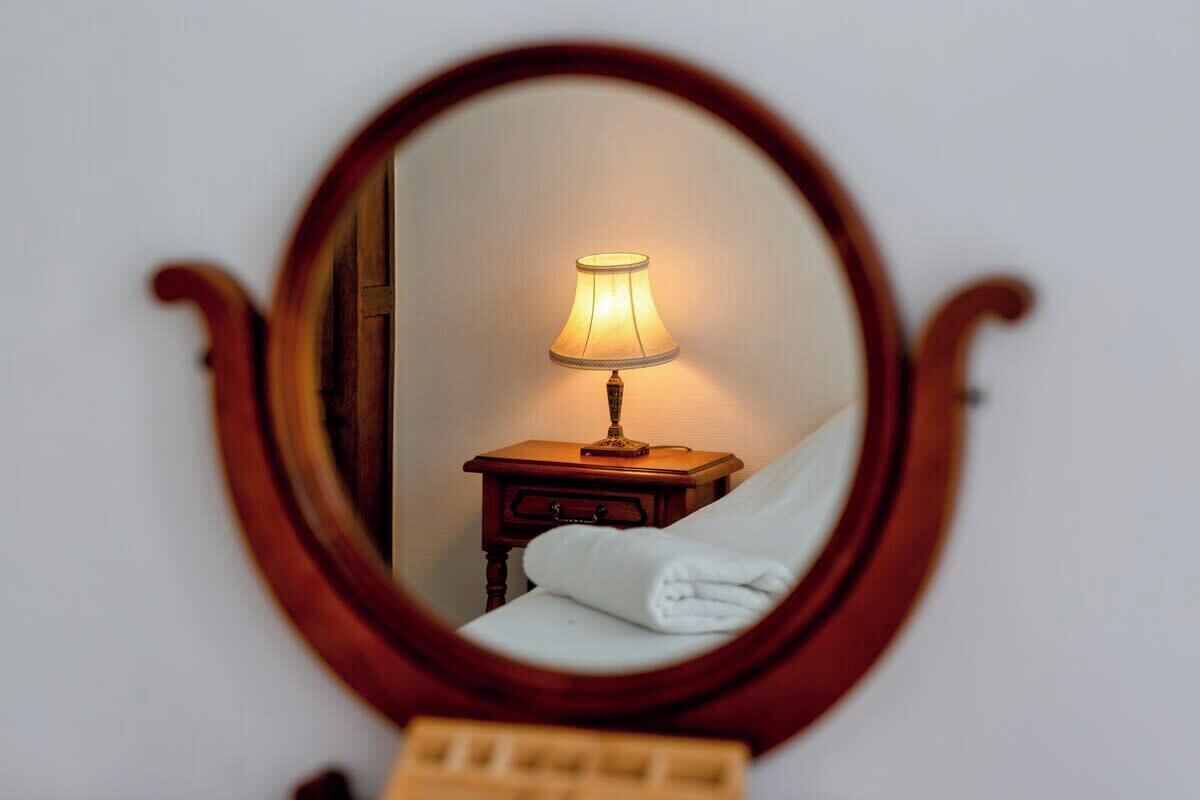 A mirror reflecting a bedside table with a lamp and a folded white towel.