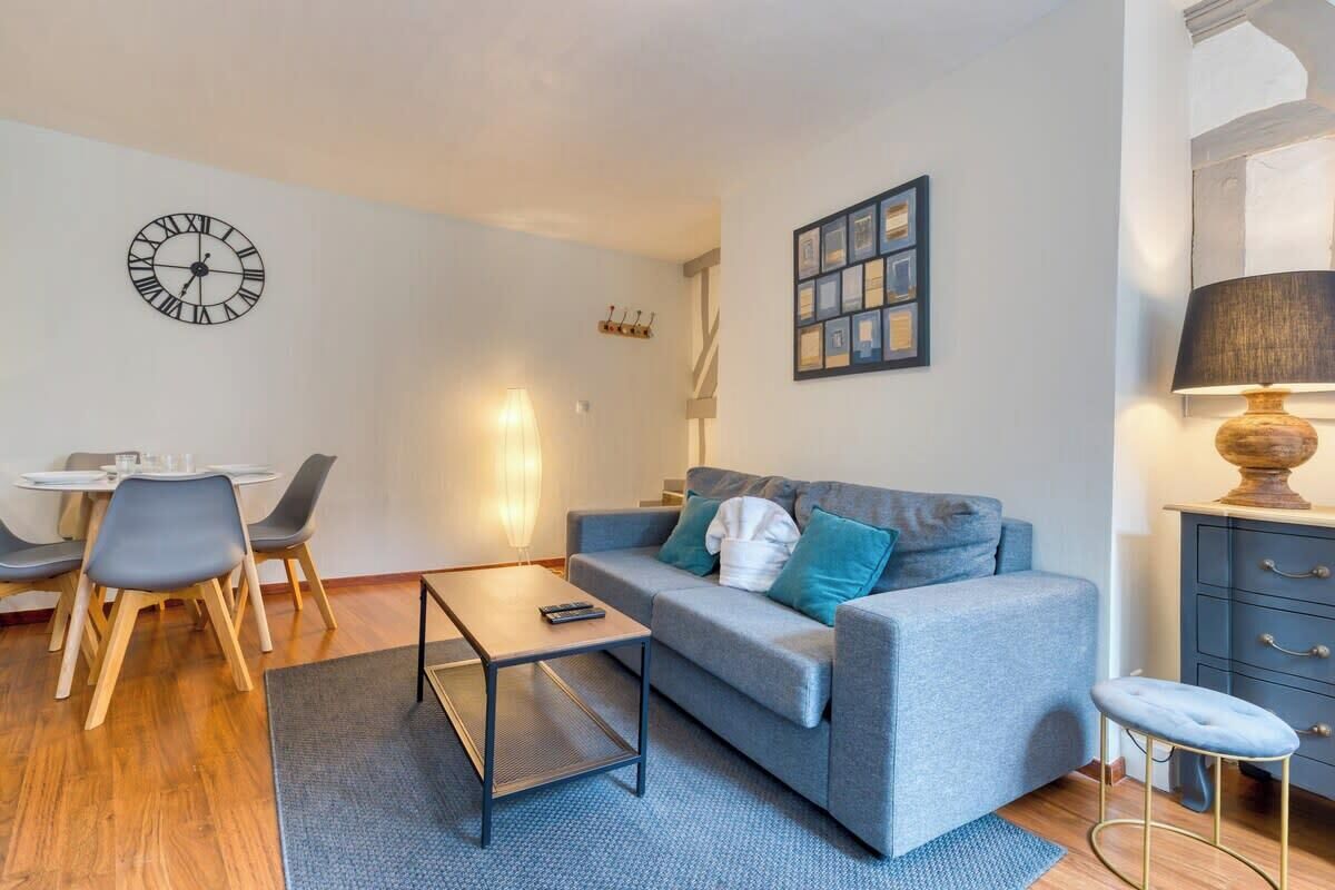 A modern living room with a grey sofa, a coffee table, a dining table with chairs, a wall clock, and a framed picture.