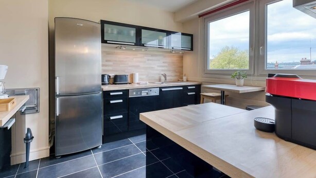 A modern kitchen with a stainless steel refrigerator, black cabinets, a wooden countertop, and a window with a view of the city.