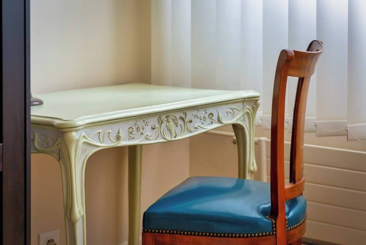 A chair with a wooden backrest and a blue cushioned seat, positioned next to a light-colored table with ornate carvings.