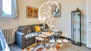 Ein Wohnzimmer mit grauem Sofa, einem Couchtisch und einem gemusterten Teppich. An den Wänden hängen zwei Bilder und eine Vitrine mit Dekoration.
