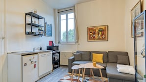 Ein kompakter Wohnbereich mit Küchenzeile, einer Couch, einem kleinen Tisch und einem gemusterten Teppich.