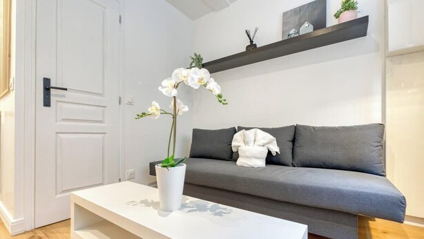 Una sala moderna con un sofá gris, una mesa de centro blanca y una planta de orquídea blanca.