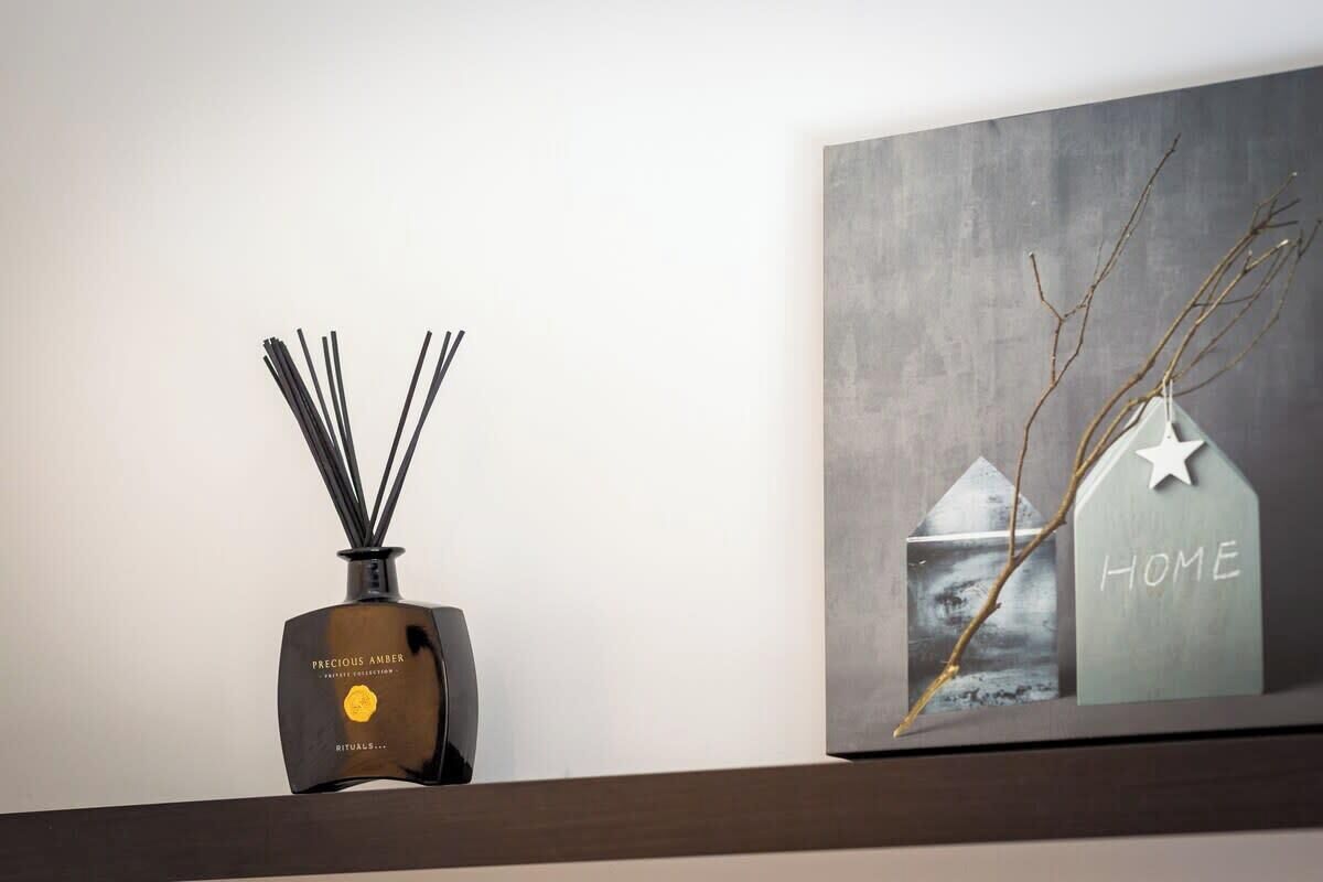 Un diffuseur mural avec une étiquette, un tableau encadré représentant une maison et une étoile, et une branche.