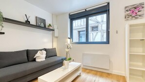 Una sala de estar moderna con un sofá gris, una mesa de centro blanca y un ventanal con vistas a edificios.