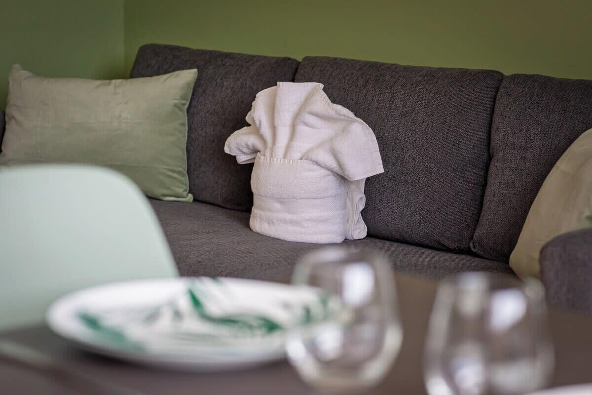 Un canapé gris sur lequel est posé un drapé blanc, un coussin vert et une assiette ornée d’un motif vert, le tout sur une table placée devant le canapé.
