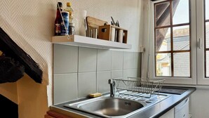 A kitchen with a stainless steel sink, a dish rack, and a window with a view of the outside. - Vera : Studio Confortable sous les combles ! (Rouen)