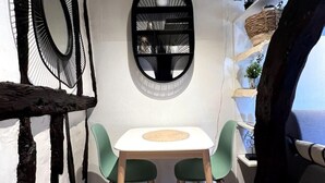 A small, cozy dining area with a round table and two chairs, a black-framed mirror, and a shelf with decorative items. - Vera : Studio Confortable sous les combles ! (Rouen)