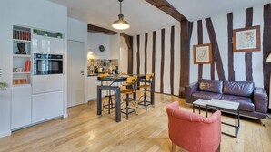 A modern kitchen with white cabinets and a dining area with wooden chairs. There is a leather sofa and a red chair in the living area.