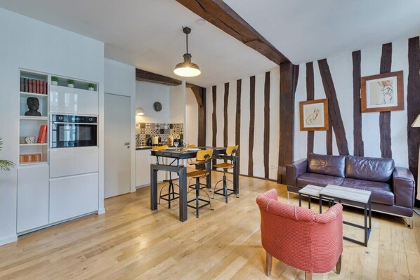 Une cuisine moderne avec des meubles blancs et un coin repas doté de chaises en bois. Le salon comprend un canapé en cuir et un fauteuil rouge.