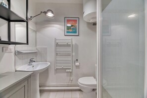 Une salle de bain moderne avec un lavabo, des toilettes et un porte-serviettes blancs. Une affiche est visible sur le mur.