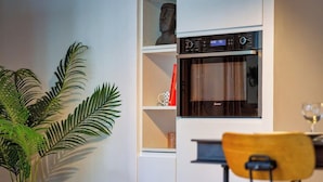 A kitchen with a built-in oven, a plant, and a dining area with a chair and table.