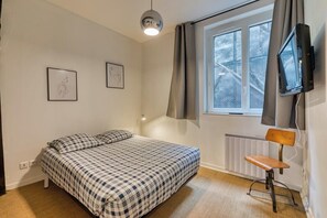 Une chambre à coucher avec un lit, une chaise, un téléviseur et deux tableaux encadrés accrochés au mur.