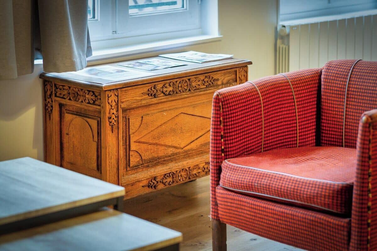 Een houten bureau met papieren, een rode geruit stoel en een raam met gordijnen.