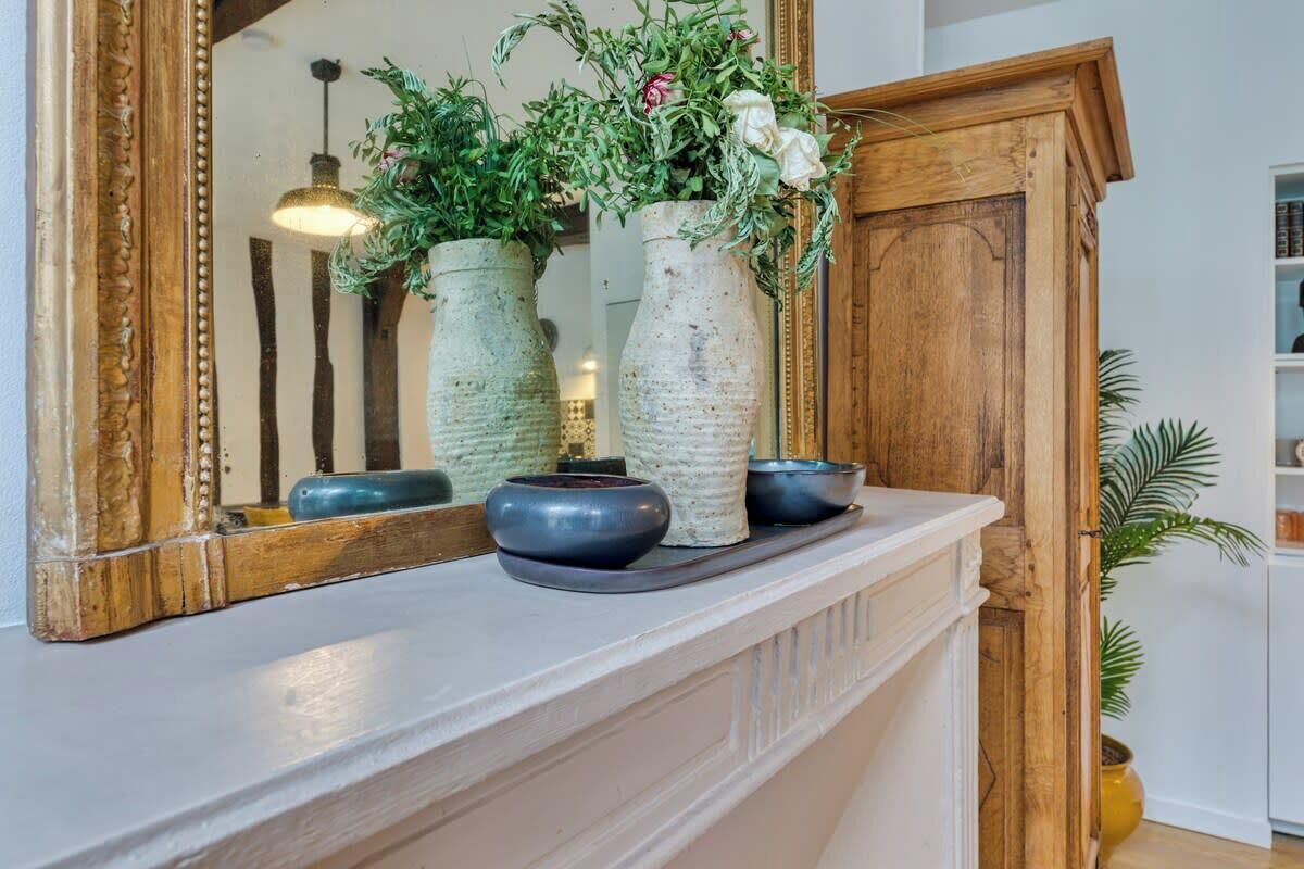 A white mantelpiece with three vases, a mirror, and a wooden cabinet.