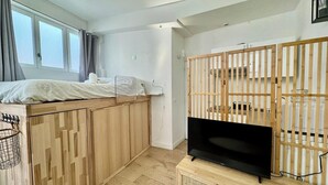 Een ruimtelijk ingerichte leefruimte met een bed, een televisie en een houten scheidingswand.