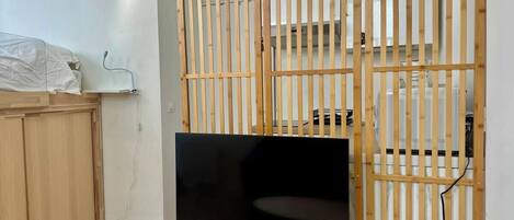 Une pièce avec un téléviseur posé sur un meuble en bois, une armoire et une cloison composée de lattes verticales.