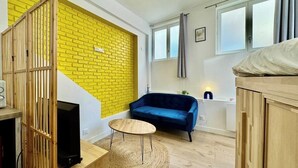 Een kamer met een geel bakstenen muur, een blauwe bank, een ronde houten tafel en een houten kast.