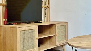 Een houten tv-meubel met een flatscreen-televisie, twee rieten opbergvakken en een ronde houten tafel.