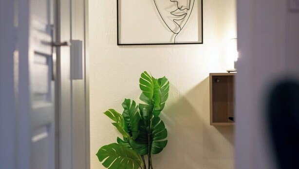Un couloir avec une plante en pot, une œuvre d’art encadrée et un plancher en bois.