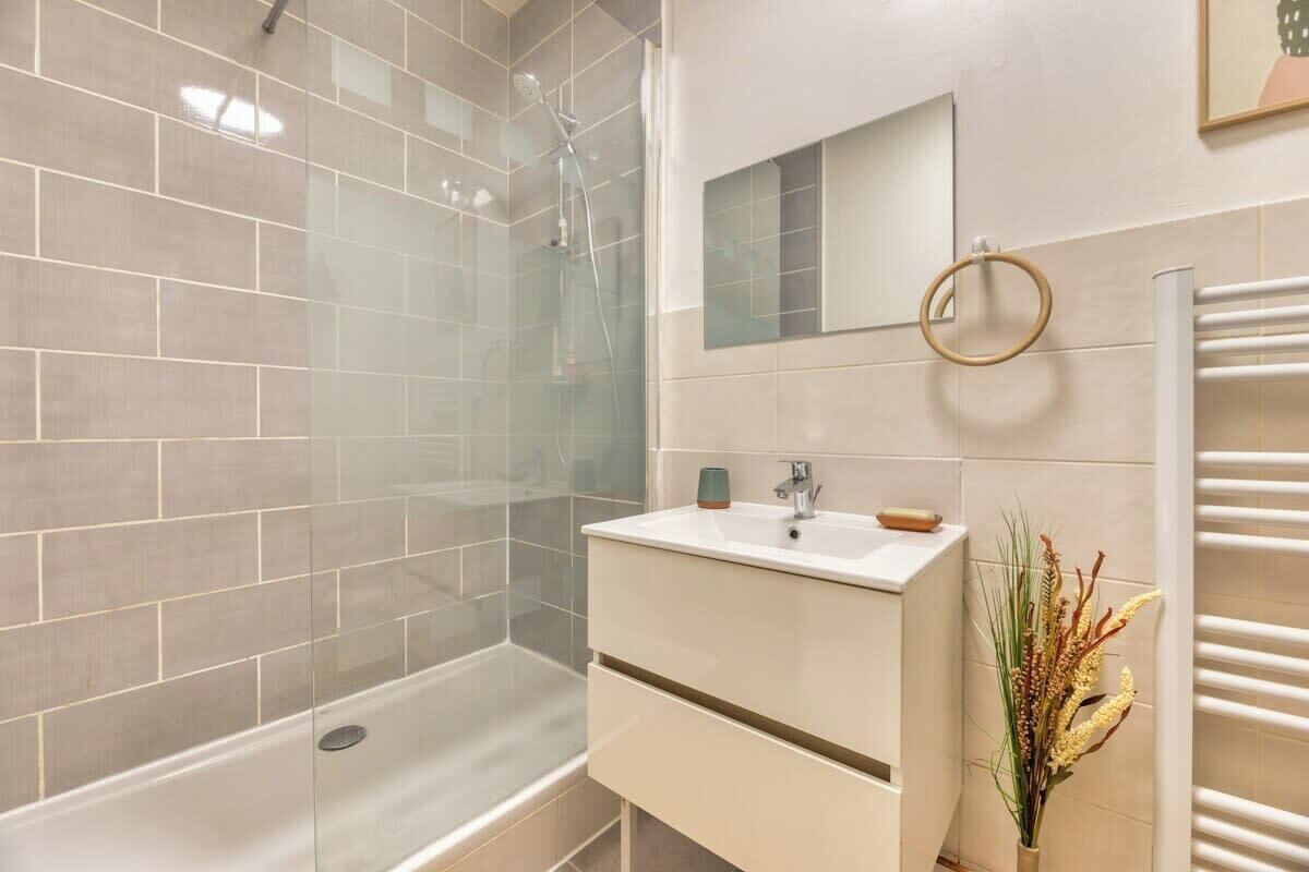 Een moderne badkamer met een douche met glazen wand, een witte wastafel met spiegel en een handdoekhouder.