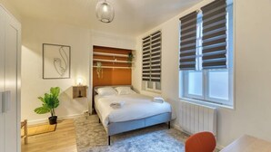 Une chambre moderne avec un lit, un bureau, une chaise, une plante en pot et une fenêtre avec des stores.