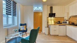 Une cuisine moderne avec des meubles blancs, un four à micro-ondes et une machine à café. On y trouve également un coin repas avec une table en verre et deux chaises.