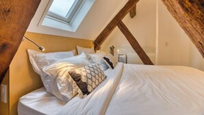 Een slaapkamer met een schuine kap, dakraam en een bed met witte beddengoed en kussens met een patroon.