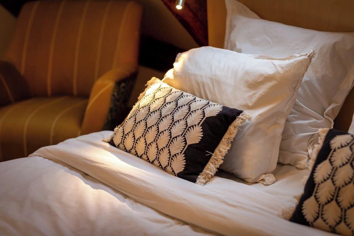 A bed with white bedding and patterned pillows, a striped armchair, and a wooden headboard.