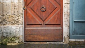 Une porte en bois ornée d’un motif en losanges et dotée d’un heurtoir en laiton, encastrée dans un mur de pierre sur lequel est fixée une plaque portant l’inscription « LOGIS S. ELOI 20 ».